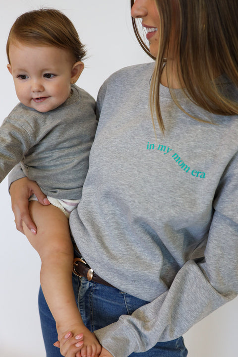 Detalle delantero de la sudadera Ondas gris junto a prenda de bebé