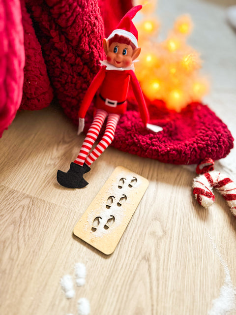 Plantilla de madera para crear huellas de elfo junto a un elfo navideño